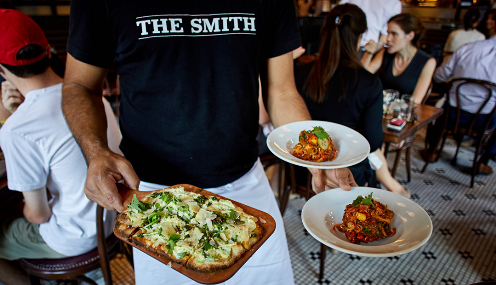 A photo of a runner at The Smith carrying several plates of food